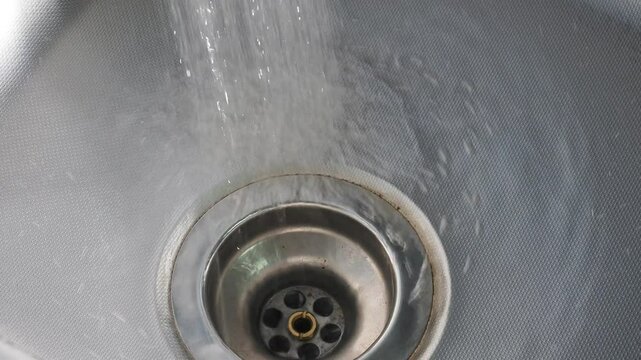 Clean water pours uselessly into a metal sink in the kitchen close-up waste of water