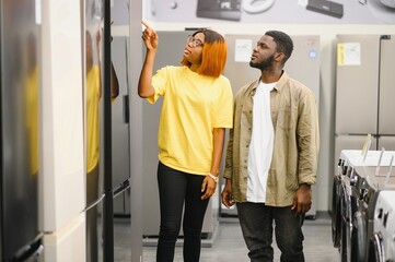 African american family couple buying domestic refrigerator in supermarket