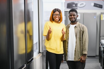 Young african american man and woman are choosing a fridge in an appliance store.