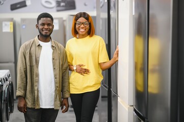 Young african american man and woman are choosing a fridge in an appliance store.
