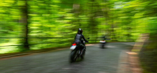 Motorcyclists navigate a winding road through a lush green forest during a sunny afternoon ride