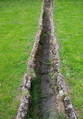 Historical drainage ditch in a green landscape showing aged stonework and natural overgrowth