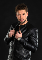 Young man poses confidently in a stylish black leather jacket against a dark backdrop during a studio photoshoot