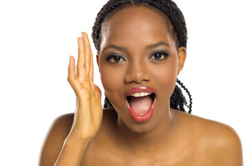 Black woman expressing surprise or shock with open mouth and raised hand, studio shot on white...