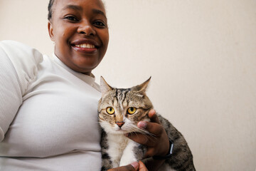 Closeup portrait, young black african American woman holding and petting adorable tabby cat at home. Positive people emotional in love pet animal, facial expression, feelings.