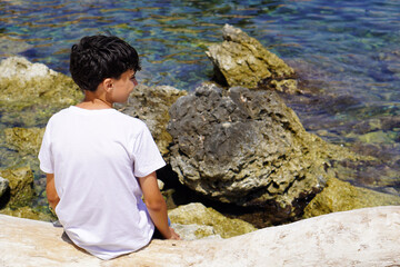 Preteen Boy Sitting on Rocks by River or Sea During Outdoor Vacation