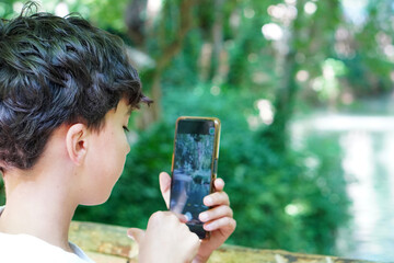 Preteen Boy Taking Photos with Smartphone by Lakeside in Nature