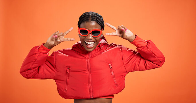 Sunglasses, excited and black woman with peace sign for fashion, style or trendy. Happy African model, studio or v hand gesture for victory symbol, emoji or cool influencer laugh on orange background