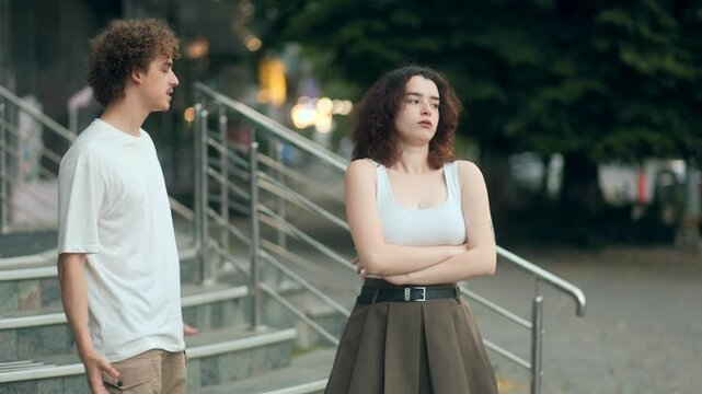 Young couple arguing outdoors, man trying to explain while woman appears upset and unresponsive