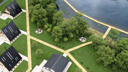 Aerial view of modern modular houses located on a coastal shoreline. Minimalist wooden cabins arranged in a geometric layout by the water, surrounded by sand and natural landscape. 