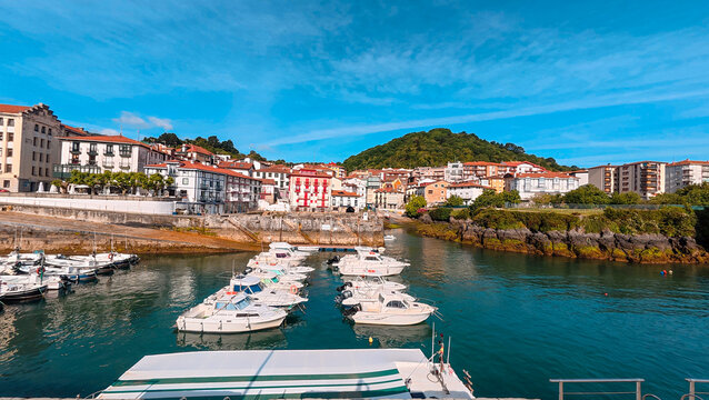 Vibrant view of the picturesque fishing port of Bermeo in the Basque Country, Spain, with colorful traditional houses and boats moored in the harbor under a brilliant blue summer sky.