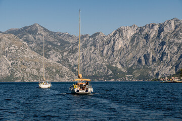 Two sailing yachts glide across the blue waters of Kotor Bay, backed by dramatic limestone...