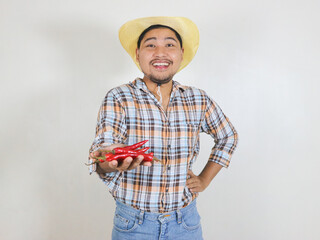 Asian male farmer wearing a rattan hat holding red chili peppers while smiling