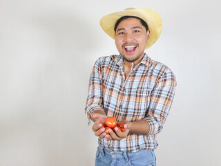 Fototapeta premium Asian male farmer wearing a rattan hat showing the tomatoes he has harvested, with an excited expression