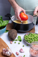 Taking a round red tomato among other vegetables for cooking.