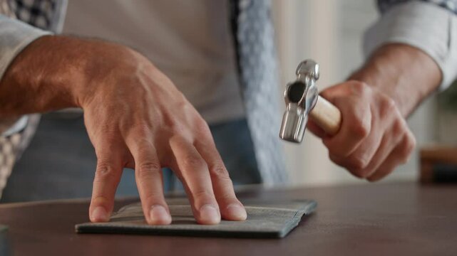 Process of softening seam on leather item, tailor uses hammer to soften craft detail.