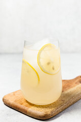 A refreshing glass of lemonade with ice cubes and lemon slices, placed on a wooden cutting board...