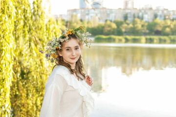 Girl in a wreath against the background of a river at sunset.