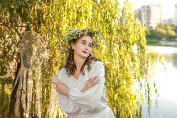 Girl in a wreath against the background of a river at sunset.