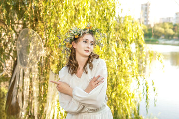 Girl in a wreath against the background of a river at sunset.