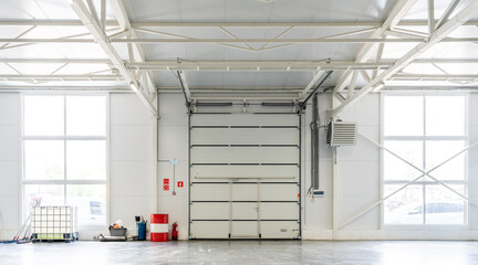Industrial warehouse with large garage door, clean concrete floor, storage containers and equipment. Logistics and manufacturing.