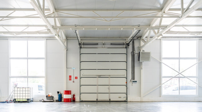 Industrial warehouse with large garage door, clean concrete floor, storage containers and equipment. Logistics and manufacturing.