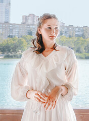 A girl in a white airy suit in a gazebo against the backdrop of a river.