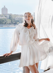 A girl in a white airy suit in a gazebo against the backdrop of a river.