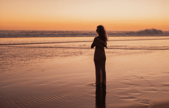 A serene moment captured at the beach with a lone figure gazing at the ocean during a beautiful sunset. The tranquil scene evokes relaxation and contemplation. - Powered by Adobe