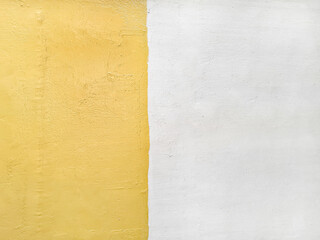 Background of the wall is painted with a vertical line separating two different colors, yellow and white. Surface texture of yellow and white walls is uneven. The wall is painted using wall oil paint.