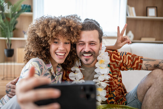 Fototapeta Happy couple wearing hawaiian garland taking a selfie at home