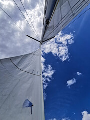 Upward view of sailboat mast and sail against a deep blue sky with scattered clouds. Ideal for...