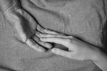 A young woman stretches her hand towards the hand of an elderly tired woman