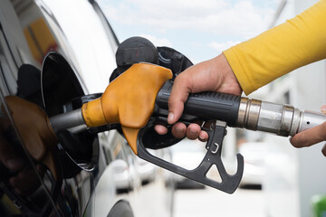 Hand holding fuel nozzle pumping gasoline into car at gas station close up showing refueling and...