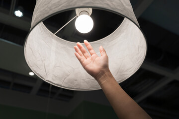 Hand reaching to touch light bulb inside lamp shade showing bright idea creativity and energy...
