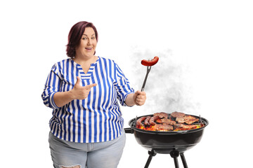 Woman grilling meat on a bbq and pointing at a sausage