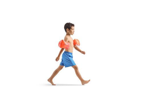 Boy in swimming shorts wearing swimming arm bands and walking