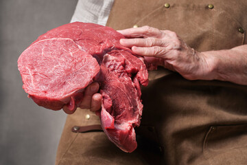 A piece of meat and the butcher's hands. Cooking. Tasty appetizing piece of fresh meat on bone in a old hands. Selective focus