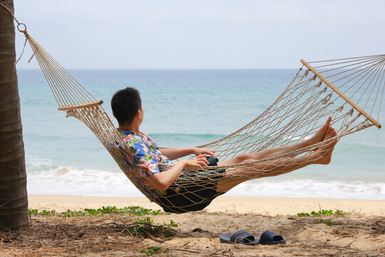 man relaxes in a hammock on the beach looking at ocean in Sanya, Hainan, China