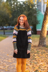 Portrait of a young beautiful cheerful red-haired girl in an evening autumn city.