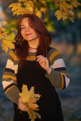 Portrait of a young beautiful cheerful red-haired girl in an evening autumn city.