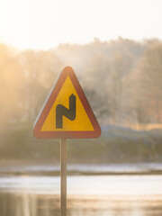 Warning sign indicating a sharp turn in a scenic area during soft morning light in Sweden's...