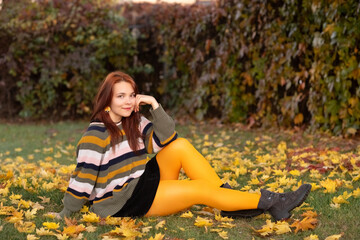 Portrait of a young beautiful cheerful red-haired girl in an evening autumn city.