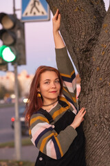 Portrait of a young beautiful cheerful red-haired girl in an evening autumn city.