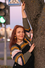 Portrait of a young beautiful cheerful red-haired girl in an evening autumn city.