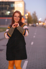 Portrait of a young beautiful cheerful red-haired girl in an evening autumn city.