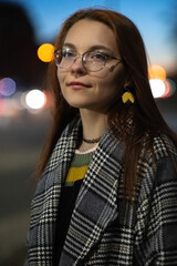 Portrait of a young beautiful cheerful red-haired girl in an evening autumn city.