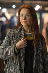 Portrait of a young beautiful cheerful red-haired girl in an evening autumn city.