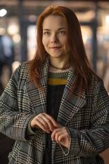Portrait of a young beautiful cheerful red-haired girl in an evening autumn city.