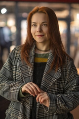 Portrait of a young beautiful cheerful red-haired girl in an evening autumn city.